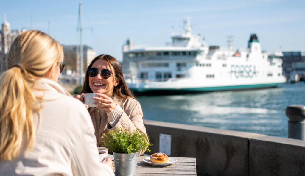 Kvinder på café ved havnen i Helsingborg med færgen mellem Helsingør og Sverige i baggrunden